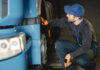 Jak bezpiecznie kupić używaną ciężarówkę z zagranicy – poradnik dla firm transportowych Mechanik w warsztacie sprawdza koło niebieskiej ciężarówki