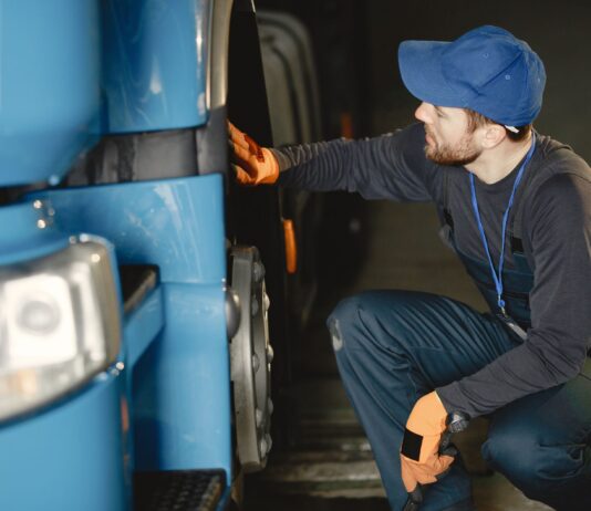 Jak bezpiecznie kupić używaną ciężarówkę z zagranicy – poradnik dla firm transportowych Mechanik w warsztacie sprawdza koło niebieskiej ciężarówki